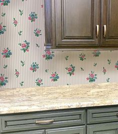 a kitchen with green cabinets and floral wallpaper on the walls, along with marble counter tops