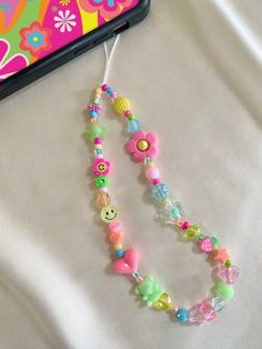 a cell phone is next to a beaded necklace on a white sheet with flowers