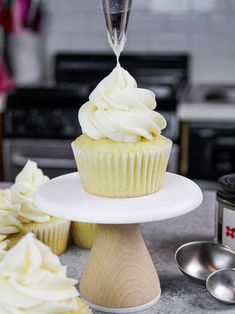 a cupcake with white frosting being poured into it on a cake stand next to other cupcakes