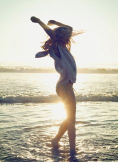 a woman standing in the ocean at sunset with her arms up and legs spread out