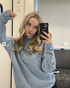 a woman taking a selfie in front of a mirror wearing a blue sweater and black leggings