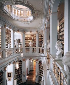 the interior of a library with many bookshelves and statues on either side of the staircase