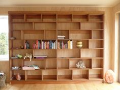 a wooden book shelf filled with lots of books next to a wall mounted vase and window