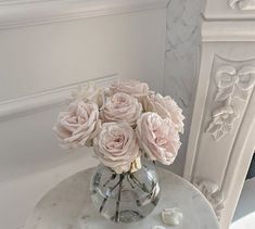 a vase filled with pink roses sitting on top of a marble table next to a fireplace