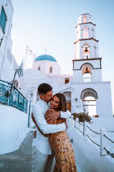 a man and woman embracing each other in front of a building with a bell tower