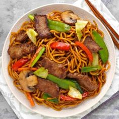 a white plate topped with noodles and meat covered in sauce next to chopsticks