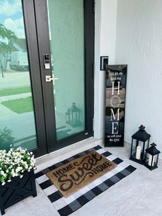 a welcome mat is on the front porch next to two lanterns and a vase with flowers