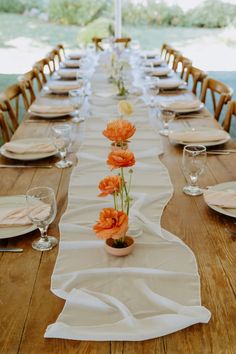 a long table is set with place settings and flowers in vases on the runner