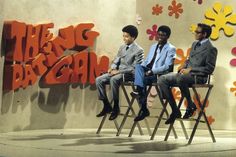 three men sitting on chairs in front of a wall