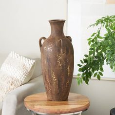 a brown vase sitting on top of a wooden table next to a white chair and potted plant