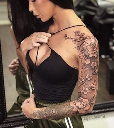 a woman with long black hair and tattoos on her arm is standing in front of a mirror