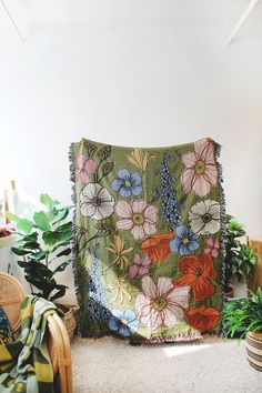 a blanket is sitting on the floor next to some potted plants and a wicker chair