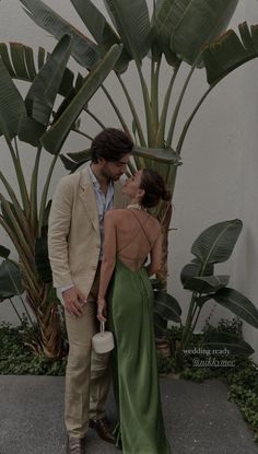 a man and woman standing next to each other in front of some palm tree leaves