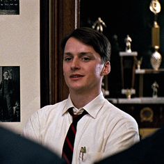 a young man wearing a white shirt and tie in front of a wall with pictures on it