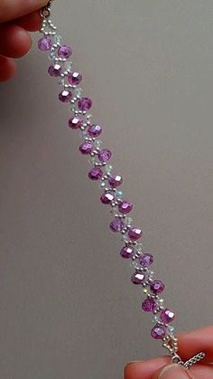 a person is holding a purple beaded bracelet with silver beads and a cross on it