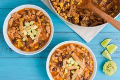 two bowls of chili chicken and corn soup on a blue wooden table with lime wedges