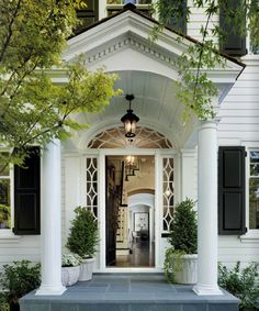 a white house with black shutters on the front door and windows in the entry way