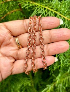 a hand holding two gold chains on it's fingers, with green plants in the background