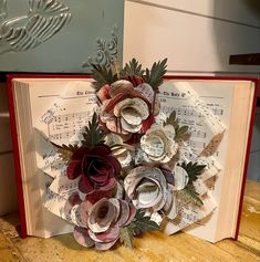 an open book decorated with paper flowers and sheet music notes is on a wooden table