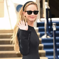 a woman in black jacket and sunglasses standing next to steps with her hand out for the camera