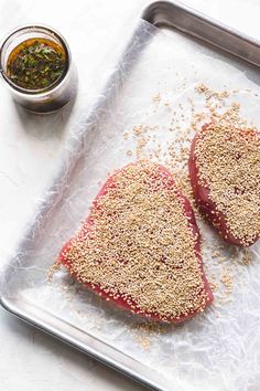 two steaks on a tray with seasoning next to it