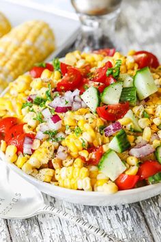 corn salad with cucumbers, tomatoes, and red onion in a white bowl