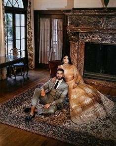 a man and woman sitting on a rug in front of a fireplace