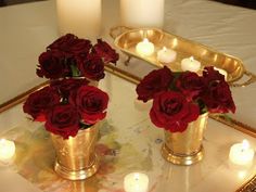 two vases filled with red roses on top of a table next to lit candles