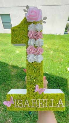 someone is holding up a moss covered number one with pink flowers and butterflies on it