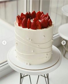 a white cake topped with strawberries on top of a table next to a window