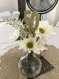 a vase filled with white flowers sitting on top of a table next to a fan