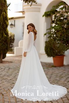 a woman in a white wedding dress standing on a cobblestone walkway with her back to the camera