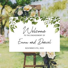 a welcome sign with white flowers and greenery on it in front of a green field