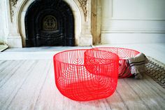 a red wire basket sitting on the floor in front of a fire place and fireplace