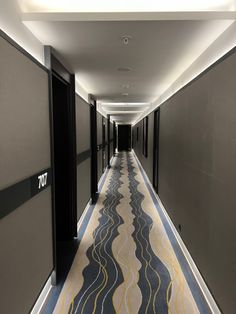 a long hallway with black doors and yellow carpet on both sides, leading to another room