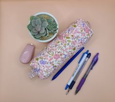 a pencil case, pen holder, and other office supplies on a pink surface with succulents