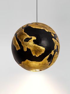 a black and gold ball shaped light hanging from a ceiling fixture with a white background