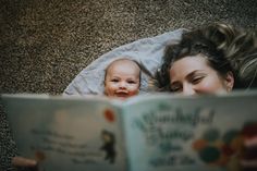 a woman laying on the floor reading a book to her baby