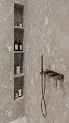 a bathroom with white and beige walls, shelves on the wall and a shower head