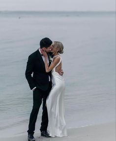 a bride and groom kissing on the beach in front of the water at their wedding