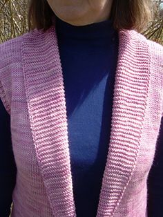 a woman wearing a pink knitted cardigan standing in front of some grass and trees