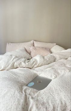 an apple laptop sitting on top of a unmade bed with white sheets and pillows