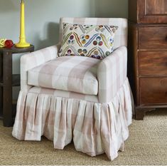 a chair with a pillow on top of it next to a lamp and dresser in a room