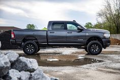 a black truck parked on top of a wet parking lot next to a pile of rocks