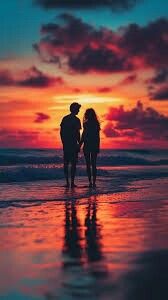 two people are standing on the beach as the sun sets in the sky behind them