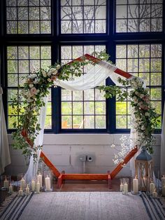 a wedding arch with flowers and candles in front of a window at the end of an aisle