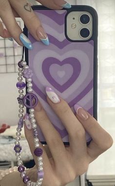 two hands holding up an iphone case with purple and white designs on the front, while another person's hand holds a beaded bracelet