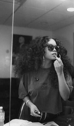 a woman sitting in front of a mirror talking on a cell phone while wearing sunglasses