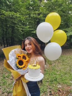 a woman holding a cake with candles and sunflowers on it in front of balloons