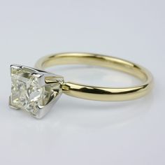 a yellow gold engagement ring with a princess cut diamond in the center, on a white background